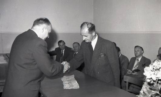 ARH NL Koberg 9372, Zwei Männer in Anzügen geben sich die Hände über einem Tisch mit Geldscheinen, mehrere Männer im Hintergrund?, Hannover, 1953