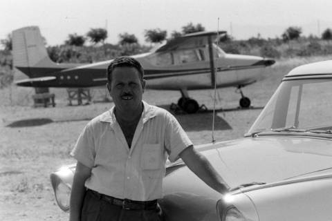ARH NL Mellin 01-088/0002, An ein Auto lehnender Mann mit einem Motorflugzeug im Hintergrund, ohne Datum