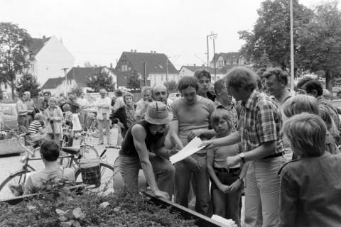 ARH NL Mellin 01-146/0011, Gruppe von Leuten mit Zetteln an einem Beet, ohne Datum