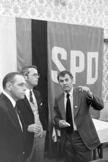 ARH NL Mellin 01-149/0019, Drei Männer in einem Gespräch vor einer Art Wandteppich mit dem Aufdruck "SPD", ohne Datum