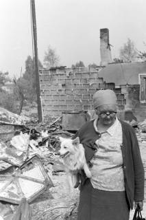 ARH NL Mellin 01-170/0005, Ältere Frau mit Hund vor einer Hausruine nach einem Waldbrand in der Heide, Hustedt, 1975
