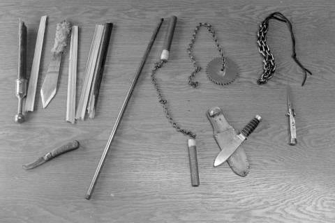 ARH NL Mellin 01-191/0012, Mehrere Waffen (u. a. Nunchucks, Messer und ein Sägeblatt an einer Kette) auf einem Tisch, ohne Datum