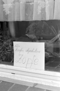 ARH NL Mellin 01-196/0001, Zettel mit der Aufschrift "Wir kaufen abgeschnittene Zöpfe" in einem Fenster eines Friseurladens, ohne Datum