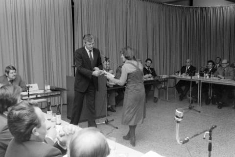 ARH NL Mellin 02-024/0005, Frau überreicht einem Mann ein Blatt Papier bei einer kleinen Versammlung, ohne Datum