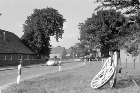 ARH NL Mellin 02-065/0002, Blick auf eine Straße in einem Dorf, rechts drei Wagenräder am Straßenrand, ohne Datum