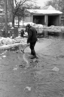 ARH NL Mellin 02-101/0003, Mann beim Reinigen des Abflusses auf einer überschwemmten Straße im Winter, um 1970