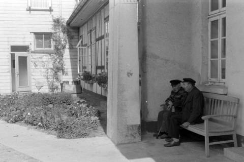 ARH NL Mellin 02-125/0007, Zwei ältere Männer auf einer Bank vor einem Wohngebäude sitzend, um 1975