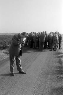 ARH NL Mellin 02-127/0016, Mann mit einer Kamera und eine Gruppe Männer auf einem Feldweg, um 1975