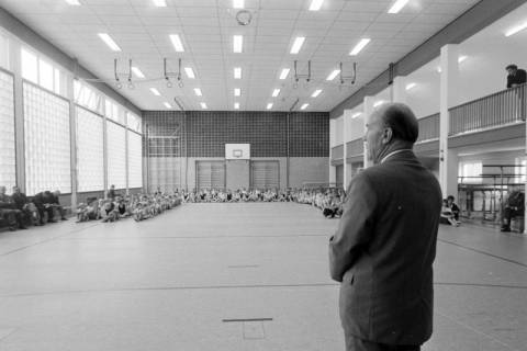 ARH NL Mellin 02-151/0017, Mann (Schuldirektor?) hält eine Ansprache vor versammelter Schülerschaft in einer Sporthalle, um 1975