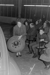 ARH NL Mellin 02-173/0005, Frau beim Radwechsel an einem Auto vor einem Publikum, um 1975