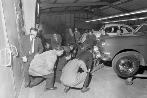 ARH NL Mellin 02-173/0012, Gruppe von Personen betrachtet ein aufgebocktes Auto in einer Autowerkstatt, um 1975