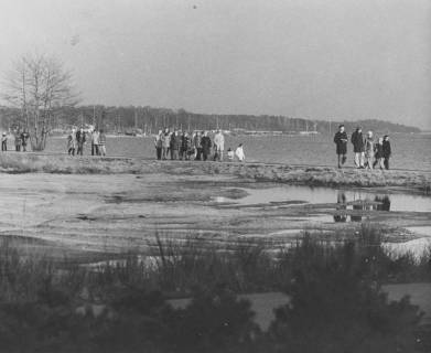 ARH Slg. Bartling 1211, Zahlreiche Spaziergänger in winterlicher Kleidung auf einem Dammweg am Ufer in der Nähe des Kurhotels (Seehotel?), Steinhuder Meer, um 1970
