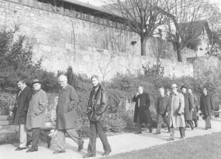 ARH Slg. Bartling 1325, Eine Gruppe von Herren schreitet über einen Fußweg unterhalb der Stadtmauer, Bad Neustadt a. d. Saale, um 1980