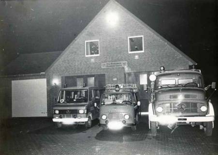 ARH Slg. Bartling 1391, Drei Feuerwehrfahrzeuge mit aufgeblendetem Licht im Dunkeln fahrbereit abgestellt vor dem Gebäude der Freiwilligen Feuerwehr, Mandelsloh-Amedorf, um 1980