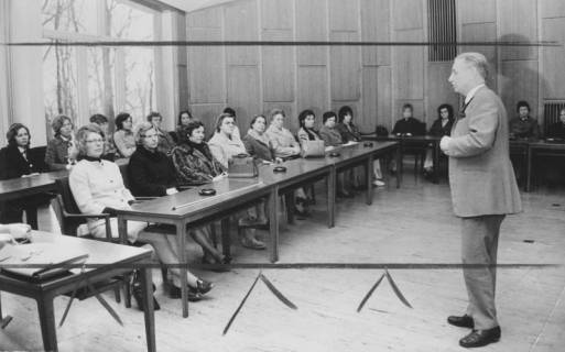 ARH Slg. Bartling 1658, Gruppe von Besucherinnen vor dem Fenster im Sitzungssaal des Kreistages an Tischen sitzend und zuhörend, rechts stehend und redend Oberamtmann Korbach, Neustadt a. Rbge., 1973