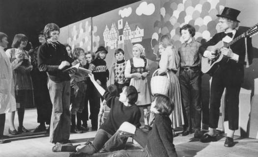 ARH Slg. Bartling 1765, Schüler spielen Theater, rechts ein Gitarrist mit Zylinder; als Kulisse dient eine Wand mit stilisierter Darstellung einer Stadtansicht und bunten Luftballons, 1974