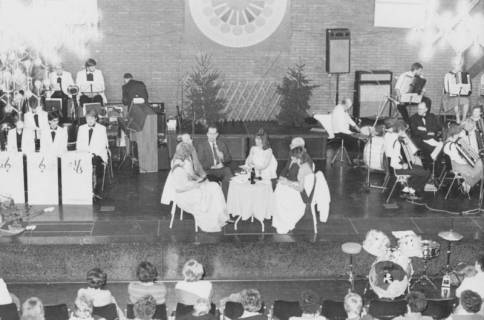 ARH Slg. Bartling 1772, Weihnachtsfeier im Saal des Freizeitzentrums, auf der Bühne in der Mitte eine Diskussionsgruppe von sechs Personen am runden Tisch, links davon eine Combo, rechts ein Akkordeonorchester, Neustadt a. Rbge., um 1975