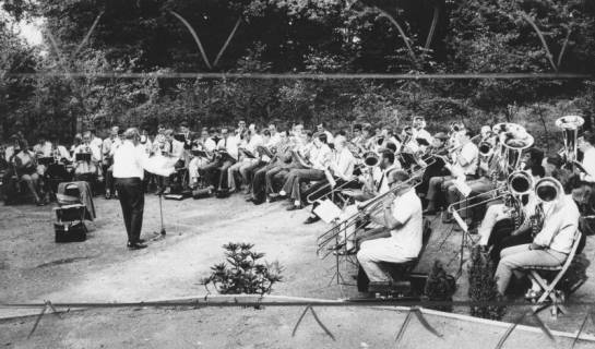 ARH Slg. Bartling 1789, Großes Blasorchester bei einem Kirchenkonzert sitzend im Halbkreis in einem Garten, Neustadt a. Rbge., 1970