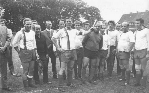 ARH Slg. Bartling 1996, Alte-Herren-Mannschaft des FC Wacker Neustadt (samt Begleitern) mit Pokal schwenkendem Spielführer Deneke locker stehend auf dem Sportplatz, Blick von vorn, 1972