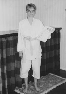 ARH Slg. Bartling 2072, Einzelporträt einer jungen Frau (S. Wiskemann ?) als Karateka im Karate-Gi mit hellem Gürtel, Brille tragend, eine Urkunde mit der Linken zeigend, in häuslicher Umgebung, um 1975
