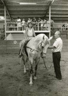 ARH Slg. Bartling 2197, Zwei Mädchen auf einem Pferd (Schimmel), das von einem Mann geführt wird, stehend beim Voltigieren in der Reithalle, Mandelsloh, um 1970