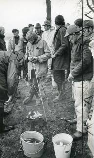 ARH Slg. Bartling 2226, Zwei Angler beim Wiegen des im Korb liegenden Fangs, im Hintergrund zahlreiche Petri-Jünger, Neustadt a. Rbge., 1974