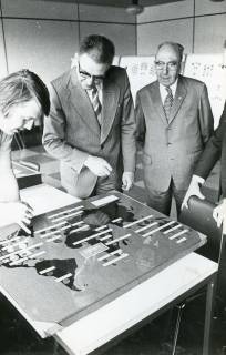 ARH Slg. Bartling 2253, Drei Männer beim Betrachten einer auf dem Tisch liegenden Tafel einer Numismatik-Ausstellung im FZZ (in der Mitte: Heinrich Schöneberg), Neustadt a. Rbge., 1974