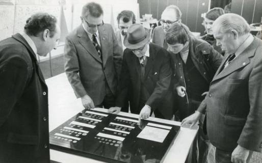 ARH Slg. Bartling 2254, Mehrere Männer beim Betrachten einer auf dem Tisch liegenden Tafel einer Numismatik-Ausstellung im FZZ (2. v. l.: Heinrich Schöneberg), Neustadt a. Rbge., 1974