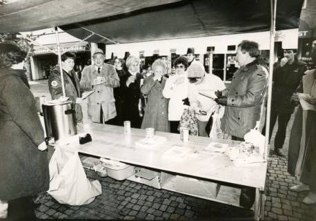 ARH Slg. Bartling 2347, DRK-Stand auf dem Weihnachtsmarkt in der Marktstraße vor der Sparkasse, Blick auf den Tisch mit Glühwein-Behälter, dahinter zahlreiche Kunden, Neustadt a. Rbge., um 1970