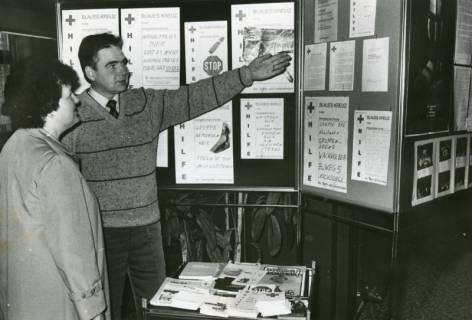 ARH Slg. Bartling 2400, Vor einer Stellwand mit Plakaten erklärt ein Mann einer Frau die Aufgabe der Selbsthilfegruppe gegen Suchtgefahren "Blaues Kreuz" der Diakonie Neustadt-Wunstorf, um 1970