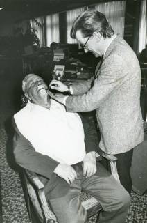 ARH Slg. Bartling 2409, Friseurmeister Klaus Fechtel (in Straßenkleidung) beim Nass-Rasieren eines Kunden in der Sparkasse, Neustadt a. Rbge., um 1975