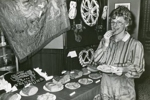 ARH Slg. Bartling 2410, Junge Frau beim Probieren der Brotsorten, die auf einer Anrichte stehen auf der Brot-Ausstellung der Bäckerinnung, Neustadt a. Rbge., um 1975