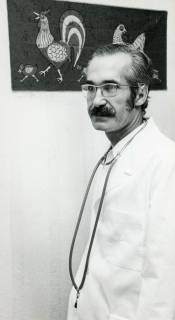 ARH Slg. Bartling 2411, Kinderarzt Dr. Suohi Ünal im weißen Kittel mit umgehängtem Stethoskopl, im Hintergrund an der Wand Bild von Hühnern in Batik-Technik, Neustadt a. Rbge., 1971