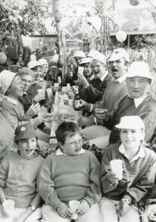 ARH Slg. Bartling 2421, Kleingärtnerinnen und Kleingärtnervmit Sonnenhut am geschmückten Tisch sitzend und dem Fotografen zutrinkend, Neustadt a. Rbge., um 1975