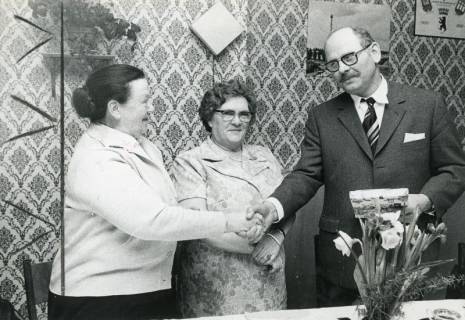 ARH Slg. Bartling 2432, August Kahle (li.) vom Reichsbund gratuliert per Handschlag zwei Frauen vor einer Wand mit geblümter Tapete, Neustadt a. Rbge., 1974