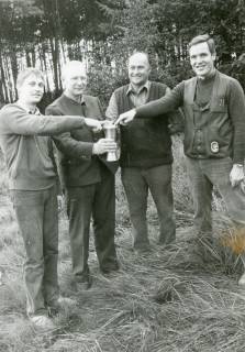 ARH Slg. Bartling 2486, Vier Männer nebeneinander auf einer Waldlichtung stehend und auf einen Pokal zeigend, Kreisjägerschaft, um 1975