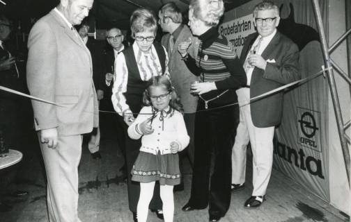 ARH Slg. Bartling 2526, Ein kleines Mädchen in Begleitung mehrerer Erwachsener durchschneidet ein Sperrband und eröffnet die Herbstmesse im Festzelt der Werbegemeinschaft, Neustadt a. Rbge., 1971