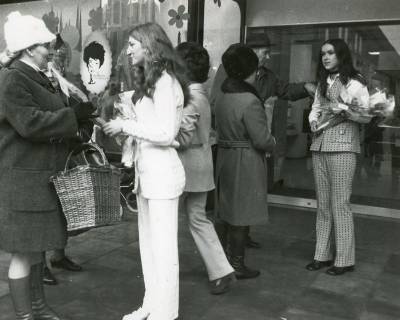 ARH Slg. Bartling 2534, Verteilung von Schnittblumen durch zwei junge Frauen im Hosenanzug an die Kundinnen vor dem Eingang des Kaufhauses Hibbe, Neustadt a. Rbge., 1971