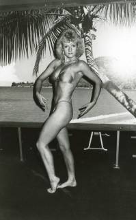 ARH Slg. Bartling 2578, Fitness-Studio, Bodybuilderin posierend mit nach unten gebogenen Armen, im Hintergrund Foto einer Palmenlandschaft, Neustadt a. Rbge., um 1975