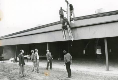 ARH Slg. Bartling 2591, Industriehalle im fertigen Rohbau, Aufziehen des Richtkranzes am Dachfirst, davor stehend fünf Männer, die den Vorgang beobachten, Neustadt a. Rbge., um 1975