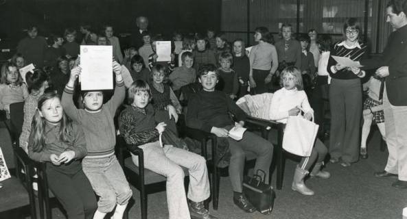 ARH Slg. Bartling 2628, Kinder sitzen im Saal des FZZ und empfangen Urkunden, die teilweise hochgehalten werden, Neustadt a. Rbge., 1974