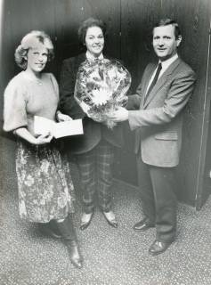 ARH Slg. Bartling 2793, Johannes Wengler, Leiter der Direktion Neustadt (r.) überreicht Frau N. N. einen Blumenstrauß in Folie, links Monika Zettlitz (Küchenstudio), Neustadt a. Rbge., um 1975