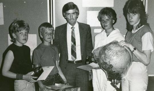 ARH Slg. Bartling 2830, N. N. von der Volksbank Neustadt gratuliert vier Schüler*innen, die vor einer Stellwand stehen, Neustadt a. Rbge., um 1973
