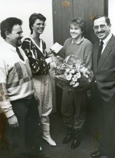 ARH Slg. Bartling 2838, Eine junge Angestellte der Dresdner Bank gratuliert einer jungen Frau mit einem Scheck und einem in Folie verpackten Blumenstrauß, daneben rechts N. N., links Schulleiter Herbert Stoepper (?), Neustadt a. Rbge., um 1973