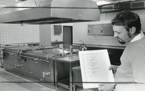 ARH Slg. Bartling 2881, Innenansicht der Kooperativen Gesamtschule (KGS), Mensa, Blick auf die blanke Kücheneinrichtung, rechts Schulleiter Herbert Stoepper mit einem Speiseplan in der Hand, Neustadt a. Rbge., 1974