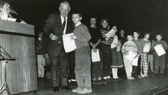 ARH Slg. Bartling 2891, Zahlreiche Grundschulkinder auf einer Bühne stehend mit einer Urkunde in der Hand, vorne Bürgermeister Henry Hahn mit einem Kind in die Kamera schauend, Neustadt a. Rbge., um 1974