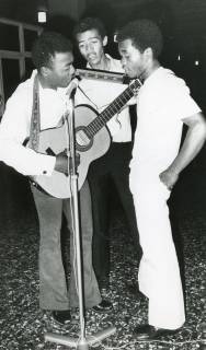 ARH Slg. Bartling 2916, Gymnasium an der Gaußstraße, Gruppe von drei afrikanischen Besuchsschülern steht und singt mit Gitarre am Mikrofon, Neustadt a. Rbge., 1972