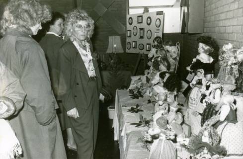 ARH Slg. Bartling 3090, Ausstellung von Hobby-Künstler*innen im FZZ, Tisch mit den Werkstücken einer Puppenmacher*in, links zwei Besucherinnen, Neustadt a. Rbge., um 1974
