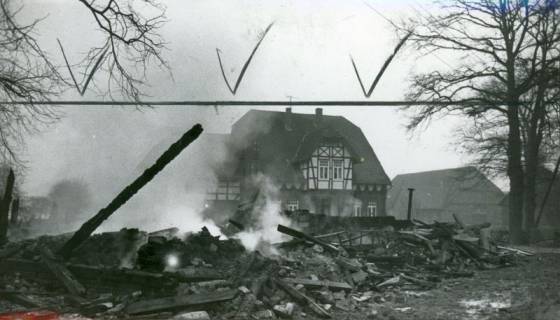 ARH Slg. Bartling 3254, Abgebranntes Haus; Blick über die qualmenden Trümmer auf ein Wohnhaus mit Fachwerk im Obergeschoss des Zwerchgiebels, Otternhagen, 1974
