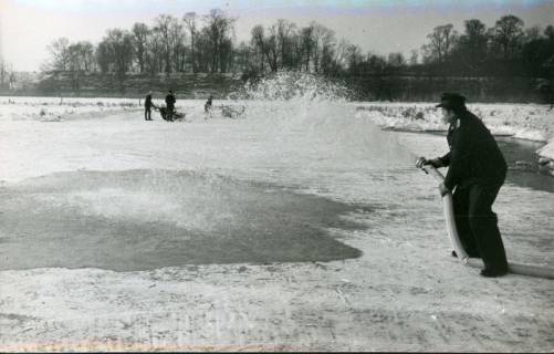 ARH Slg. Bartling 3270, Bespritzung mit Wasser aus einem Schlauch durch einen Feuerwehrmann zur Vereisung einer Fläche auf dem winterlichen Amtswerder, Blick über die Eisfläche auf die Schlossbastion, Neustadt a. Rbge., 1971